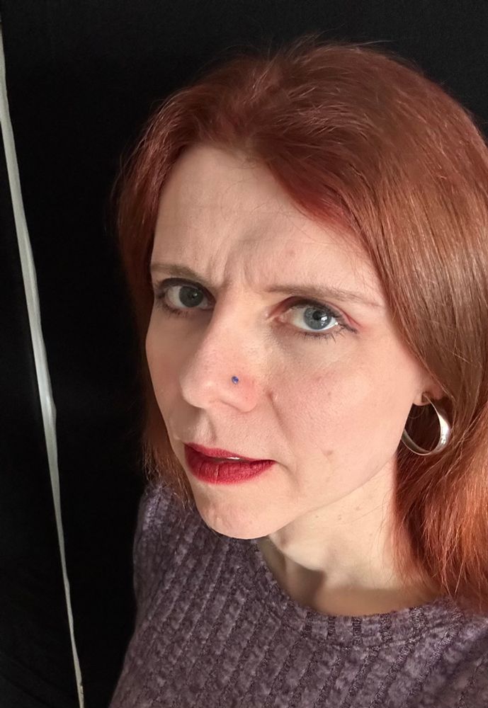 A photo of Mara. She is looking up and left towards the camera. The background is mostly black.