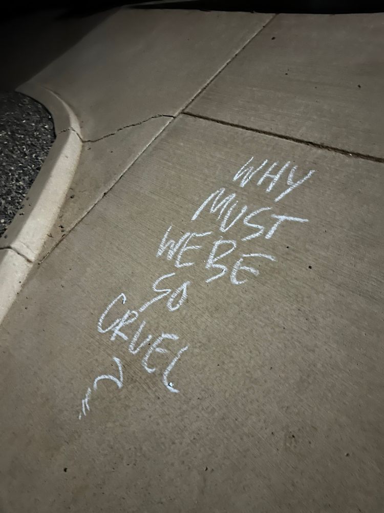 “Why must we be so cruel” written on a sidewalk 