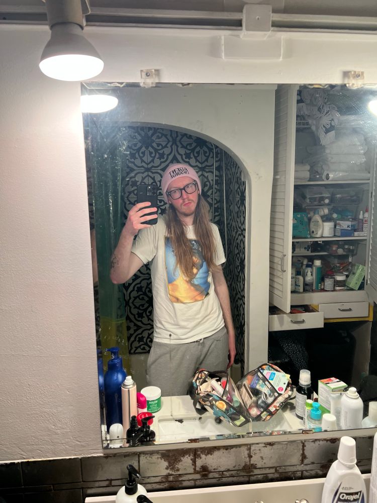 I stand in front of a mirror doin a front-cam selfie pose w my Laura Palmer shirt and my new pink agent Orange beanie w my grey sweats. There’s some makeup/bathroom detritus in frame like mouthwash but don’t worry about it. This is a face reveal btw. This is your alt-text commentary signing off 