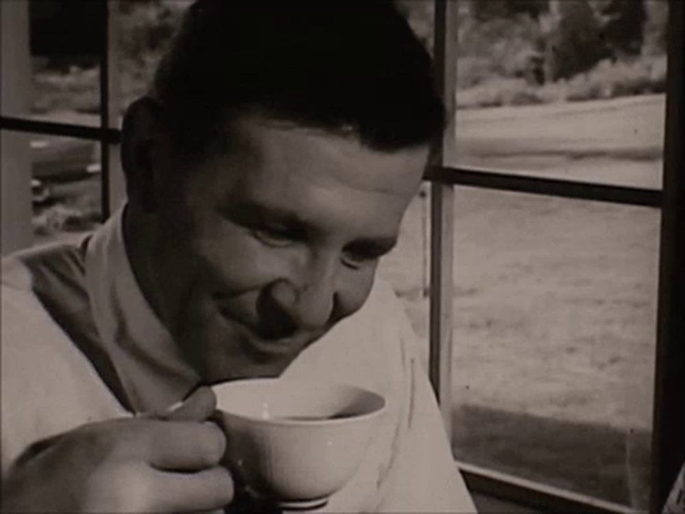 a man is drinking a cup of coffee and smiling in front of a window