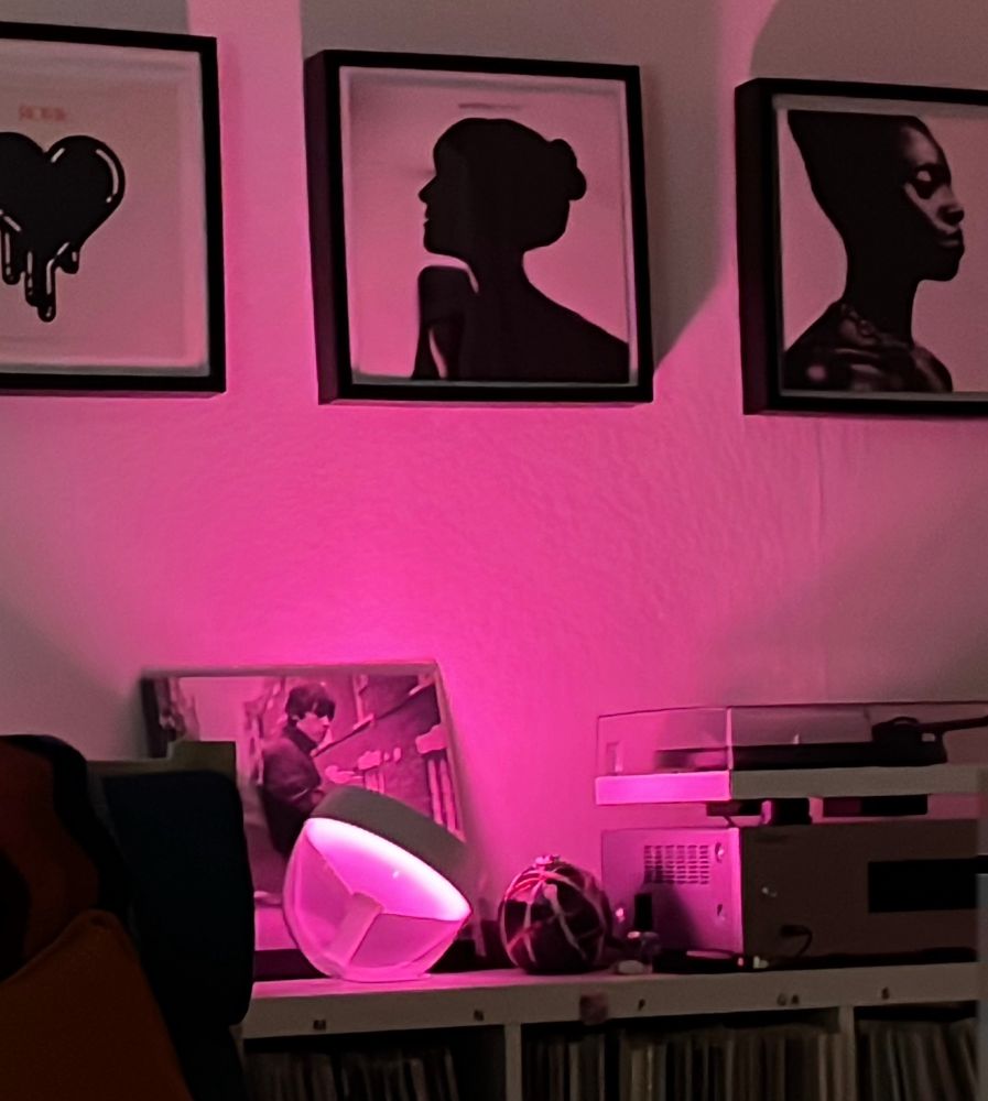 Weiße Wand pink angestrahlt. 3 Schallplatten im Rahmen davor Plattenspieler. 