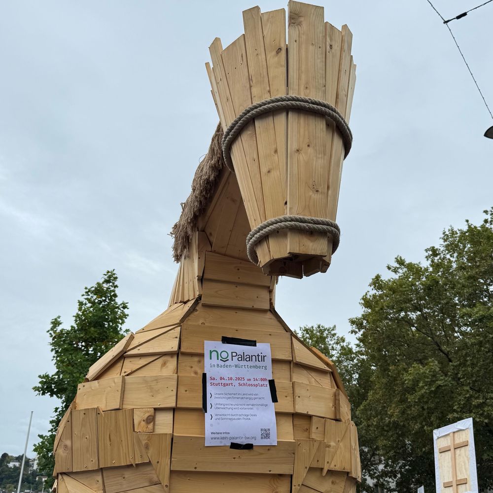 Trojanisches Pferd (Holzskulptur) mit einem Flyer der Demonstration an der Brust.