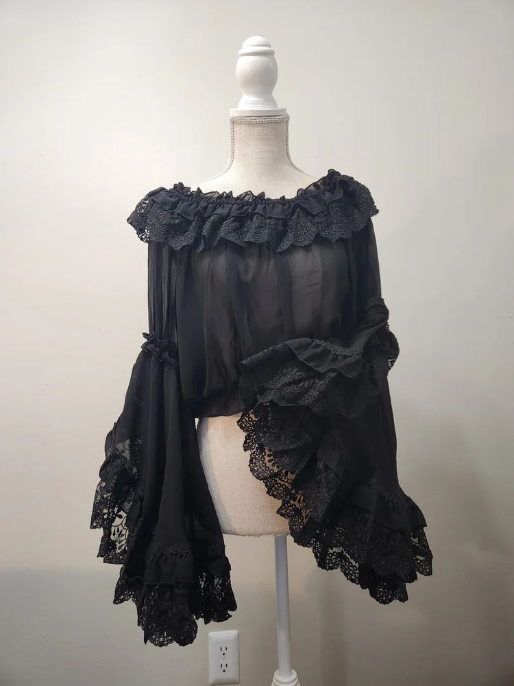 A black semi-sheer lace princess blouse. The sleeves are flounced at the elbow and trimmed with lace. The neckline is also trimmed with ruffled lace.