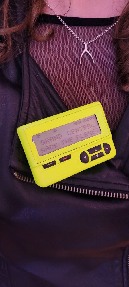 A neon yellow pager displaying the message "GRAND CENTRAL HACK THE PLANET".