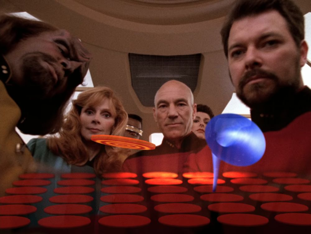 Wesley Crusher finally experiences joy as people look satisfied to find him playing a video game.