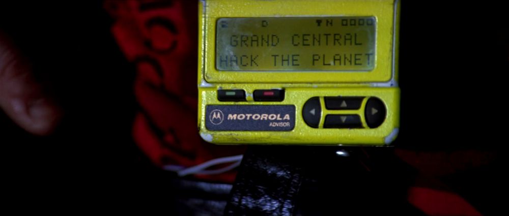 A neon yellow pager in the movie Hackers, displaying the message "GRAND CENTRAL HACK THE PLANET"
