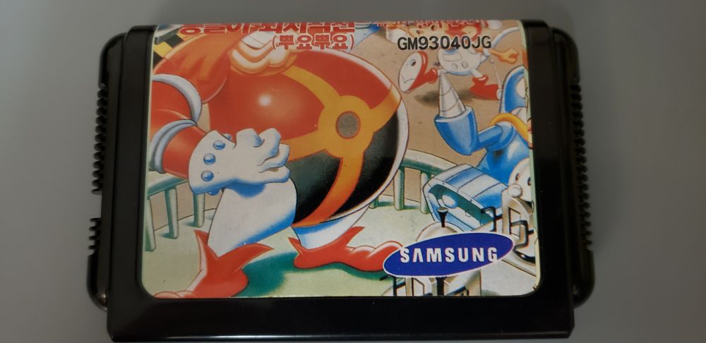 A South Korean "Dr. Robotnik's Mean Bean Machine" cartridge for the "Samsung Super Aladdin Boy," the Korean version of the SEGA Mega Drive/Genesis. It primarily shows Robotnik himself on the left, with Coconuts and Grounder also to the right but Grounder is cut-off halfway. Looking closely where this cut-off happens, we can see some kind of artwork underneath that doesn't match the Mean Bean artwork.