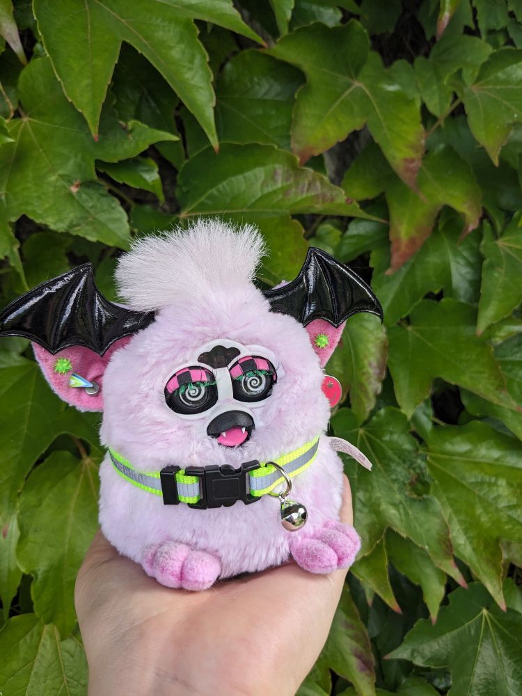 A light pink Furby baby with bat wings on their head and a custom beak