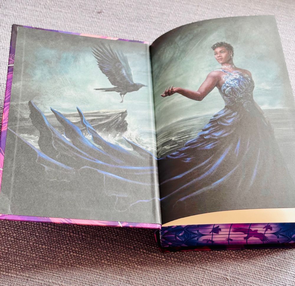 an illustrated endpaper inside the book The Raven Scholar by Antonia Hodgson.
The artwork depicts a woman in a flowing blue gown standing near the ocean, with part of her dress transforming into wave-like shapes. She is extending one hand outward toward a black raven flying near a rocky cliff. The decorative purple-and-blue stained-glass-style page edges are also visible at the bottom.