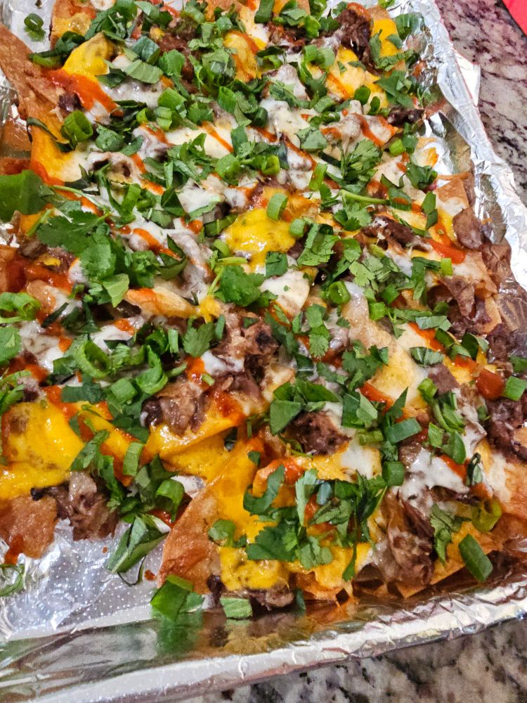A delicious platter of perfectly golden nachos topped with seasoned beef, cheese, red sauce, and lots of chopped herbs.