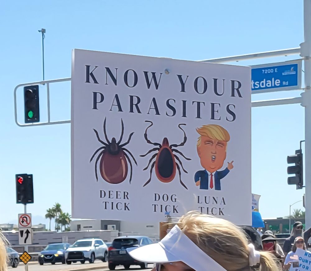 KNOW YOUR PARASITES sign: Deer Tick (pic of tick) Dog Tick (pic of tick) Luna Tick (pic of Trump)