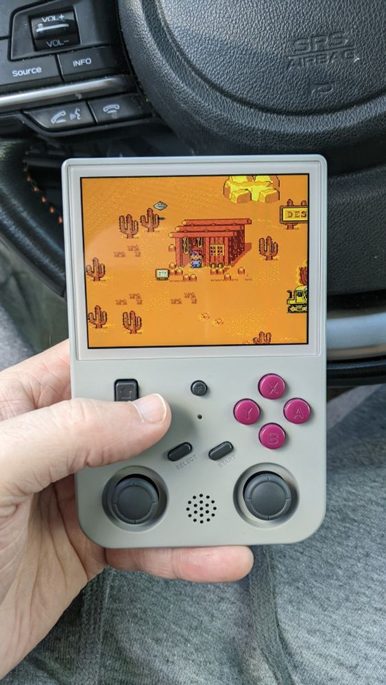 Me sitting in my car holding a Gameboy-looking handheld emulator that has earthbound playing on the screen.