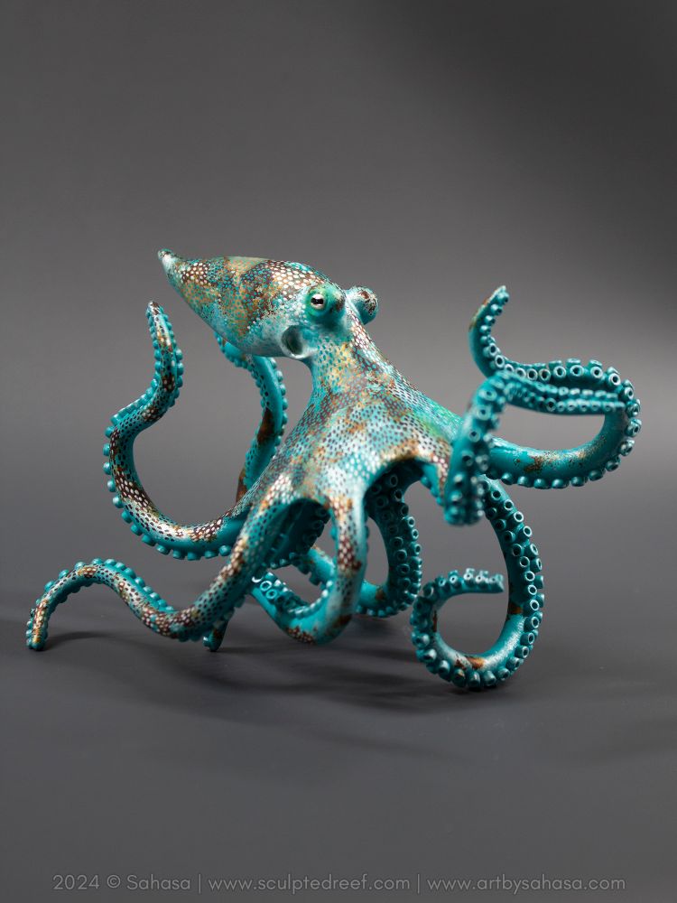 A medium size octopus sculpture that stands on its own arms, it's limbs curling outward in every direction. It looks like it's dancing.

The octopus depicts the species Caribbean Reef Octopus scientifically known as Octopus briareus. 

It's a teal-ish blue green octopus with pearly white patches, overlaid with a dotted and spotted pattern in a soft golden bronze brown. Some more subtle patches of neon green here and there complete the color palette of this sculpture.