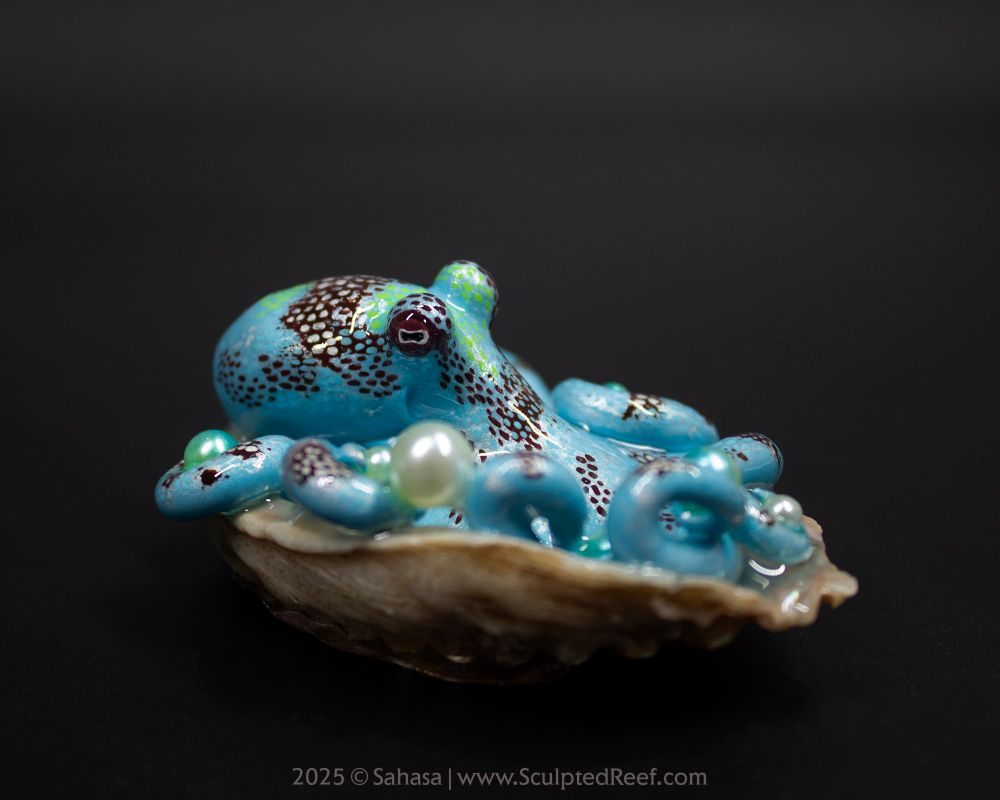 A small octopus sculpture sitting in a shell that is photographed over a black background. It's holding several faux pearls that have a matching color gradient of pearl white and bright green. The octopus depicts the species Caribbean Reef Octopus scientifically known as Octopus briareus. It's a teal-ish blue green octopus with pearly white patches, overlaid with a dotted and spotted pattern in a dark maroon brown. Some more subtle patches of neon green here and there complete the color palette of this sculpt.