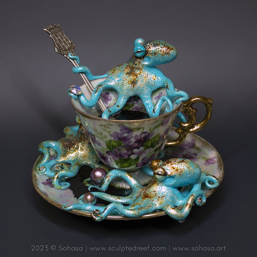 An iridescent shimmering tea cup with three hand sculpted and painted Caribbean Reef Octopuses that are playing with pearls and crystals.