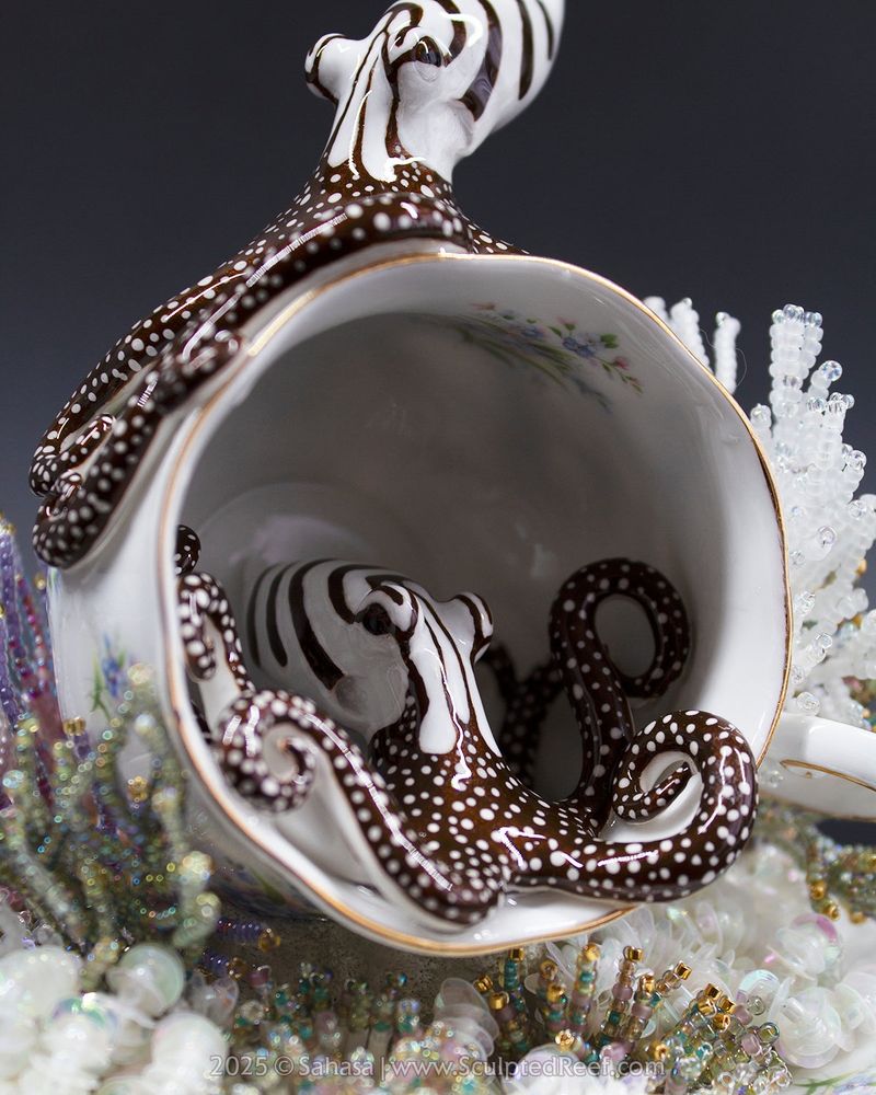 Mixed Media artwork featuring two hand sculpted and painted clay octopuses, depicting the species Larger Pacific Striped Octopus.

They're placed in and on a tea cup, which is also overgrown with colorful hand beaded corals, created from tiny glass beads set on silver wire.