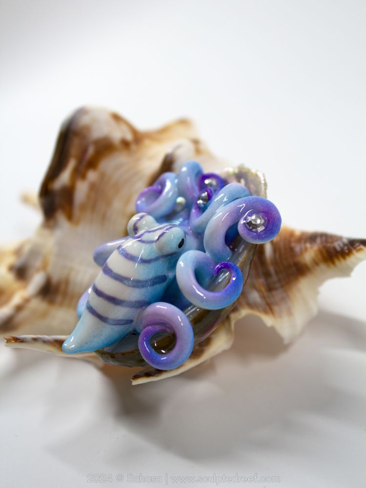 A colorful purple, blue and white octopus sculpture tucked in a shell. It's holding several Swarovski crystals..