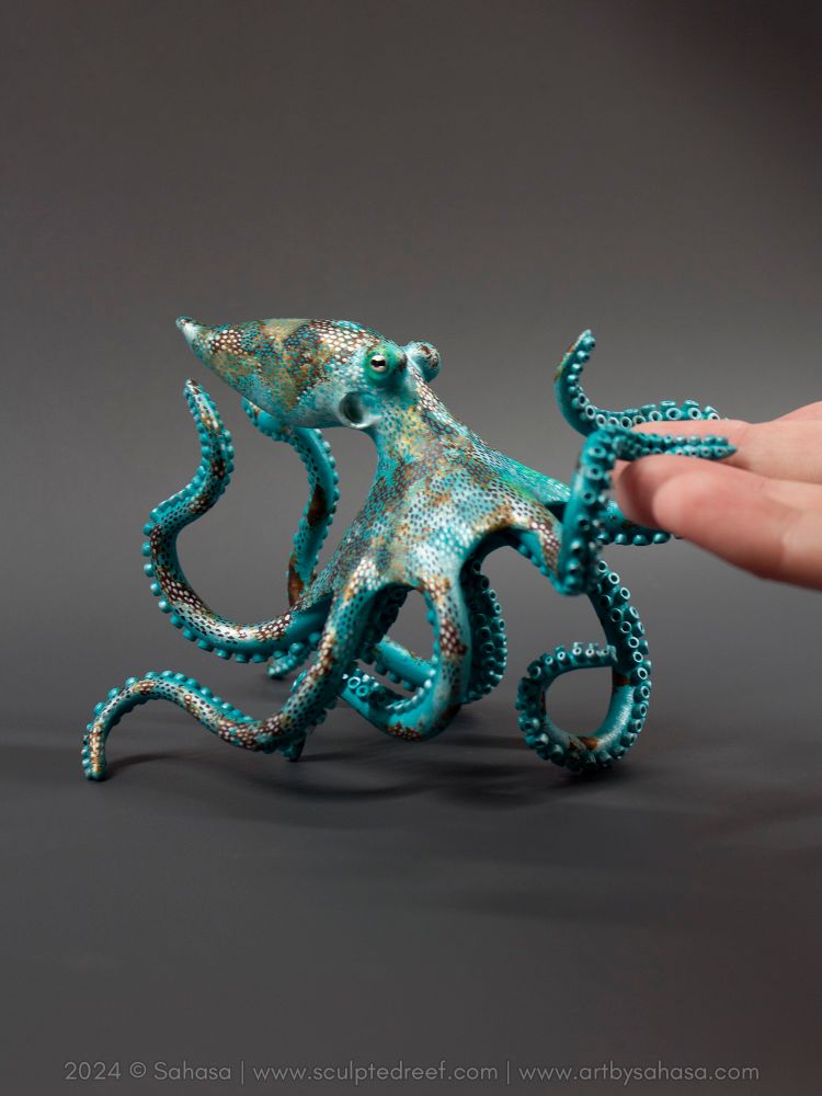 Photo of a Caribbean Reef Octopus sculpture reaching out with its arms to touch the artist's fingertips.