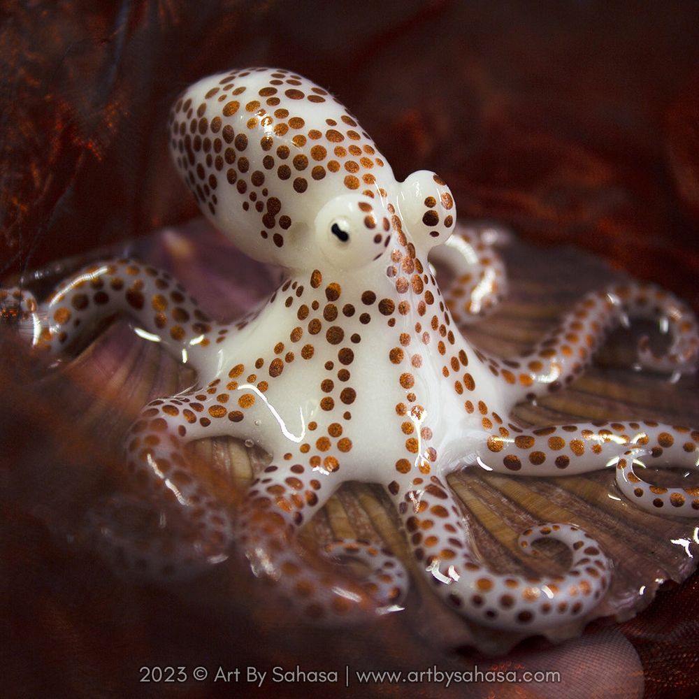 Close up of a semi transparant baby octopus sculpture, with coppery spots all over its arms and body.