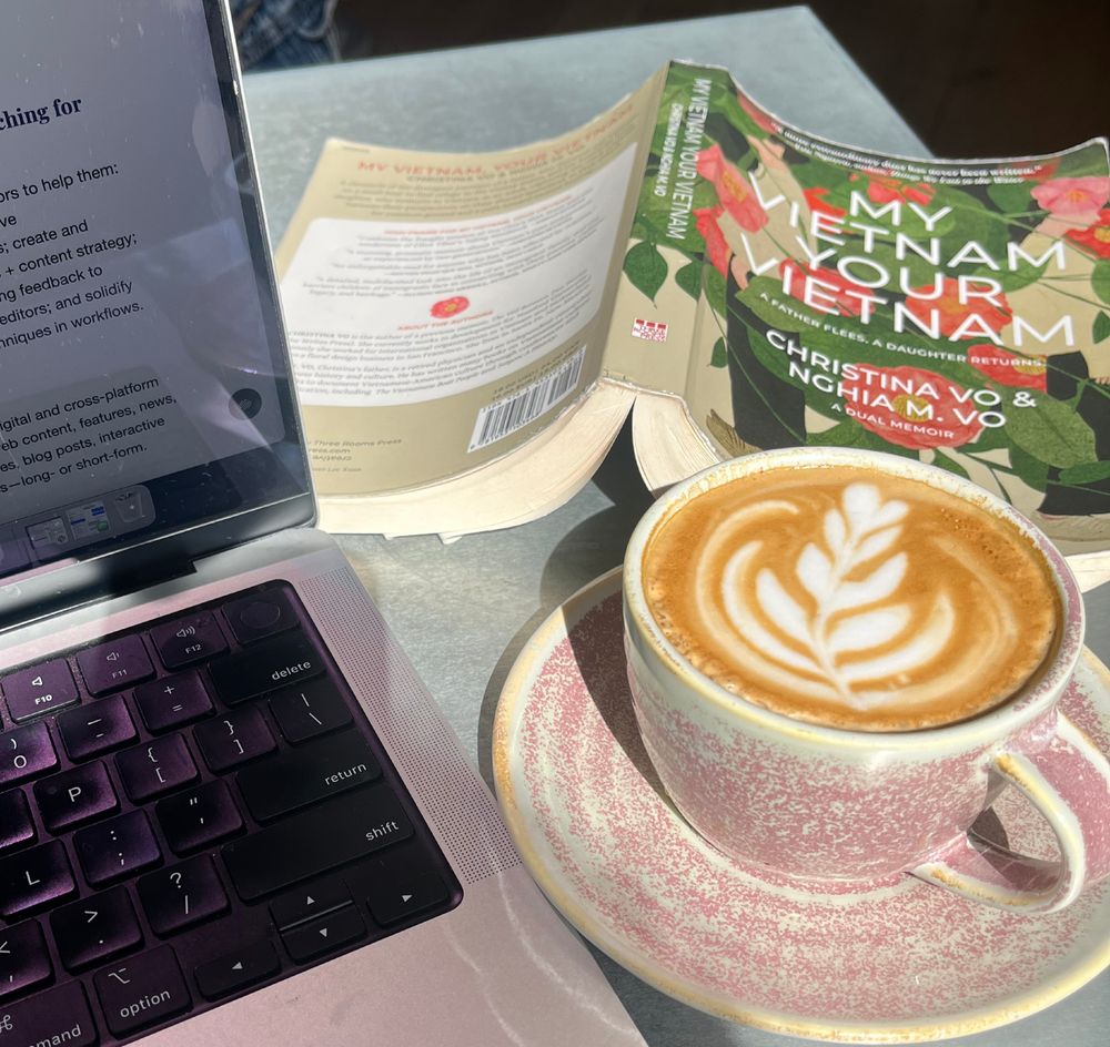 Photo of a cup of coffee, the book My Vietnam, Your Vietnam, and a laptop on a table.