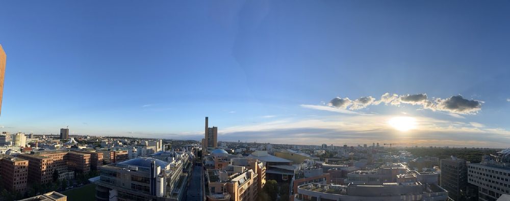 Block über die Skyline von Berlin Richtung Westen bei blauem Himmel und der Sonne hinter ein paar Wolken über den Horizont.