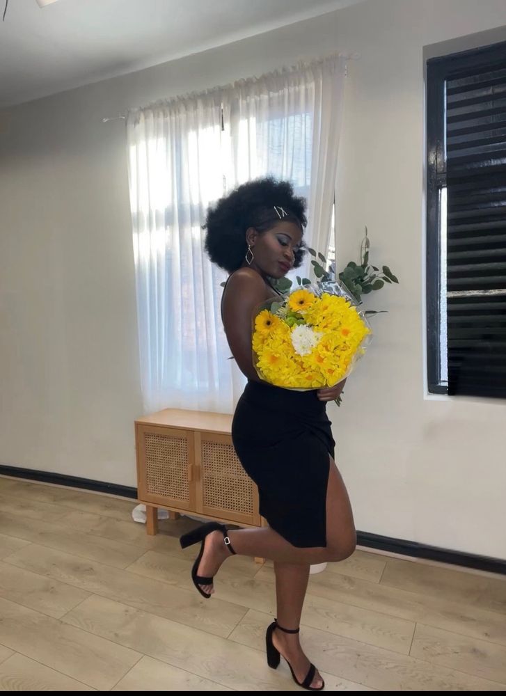 candid! me looking at flower bouquet they’re yellow and leg kicked up a little in heels in black dress during the day time 