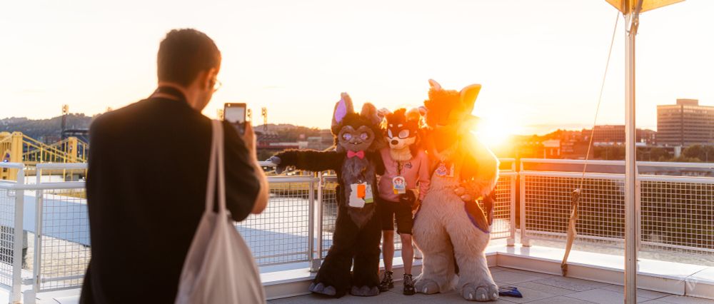 A person taking a sunset photo of fursuiters on the rooftop of the David L Lawrence Convention Center