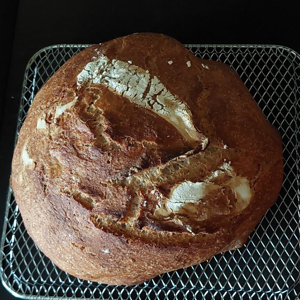 A round, crusty loaf of 75% whole wheat bread, on a cooling rack