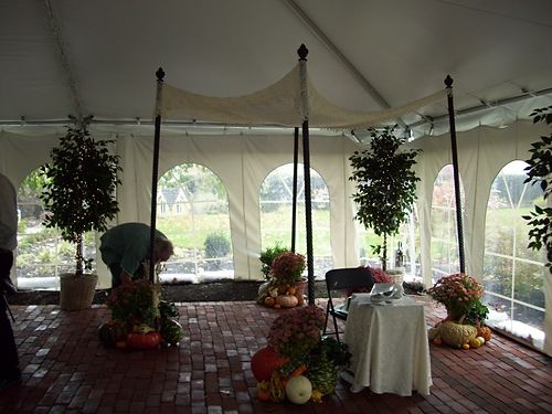 A large gathering tent with a lace chuppah on poles with autumnal gourds and flowers at the base of the pools 