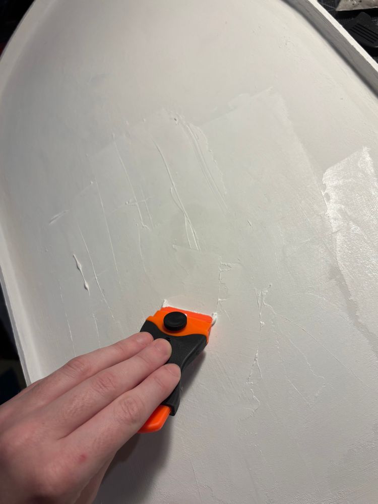 A panel being primed with a thick mix of modeling paste/gesso, using a plastic scraper to achieve a smooth surface