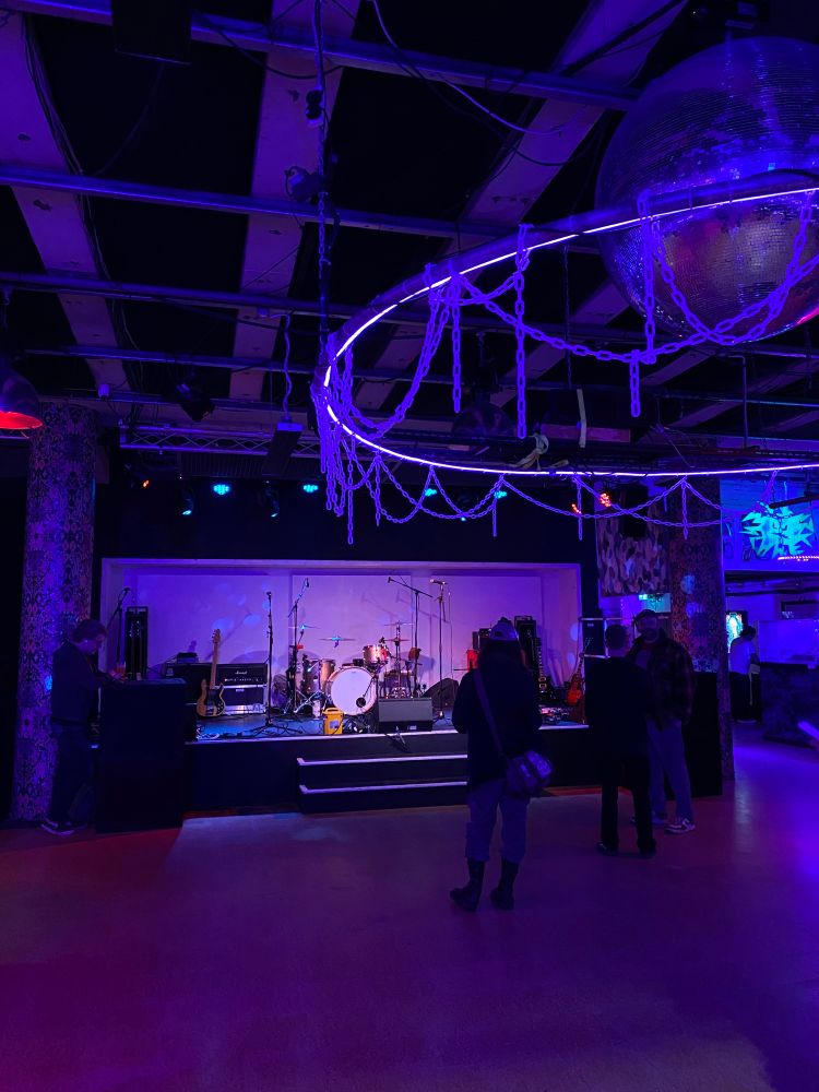 A picture of a mostly empty music venue bathed in blue light. 
The stage is set up for the support act and there's a large disco ball hanging from the ceiling