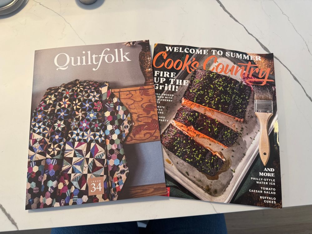 Two magazines (Quiltfolk 34: Arkansas and Cook’s Country June/July 2025) resting on a counter