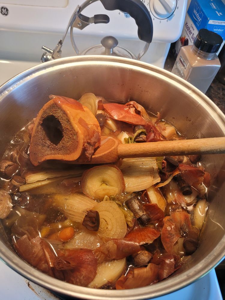 A bone is held up in a big pot filled with vegetables and water. Someone is making broth!