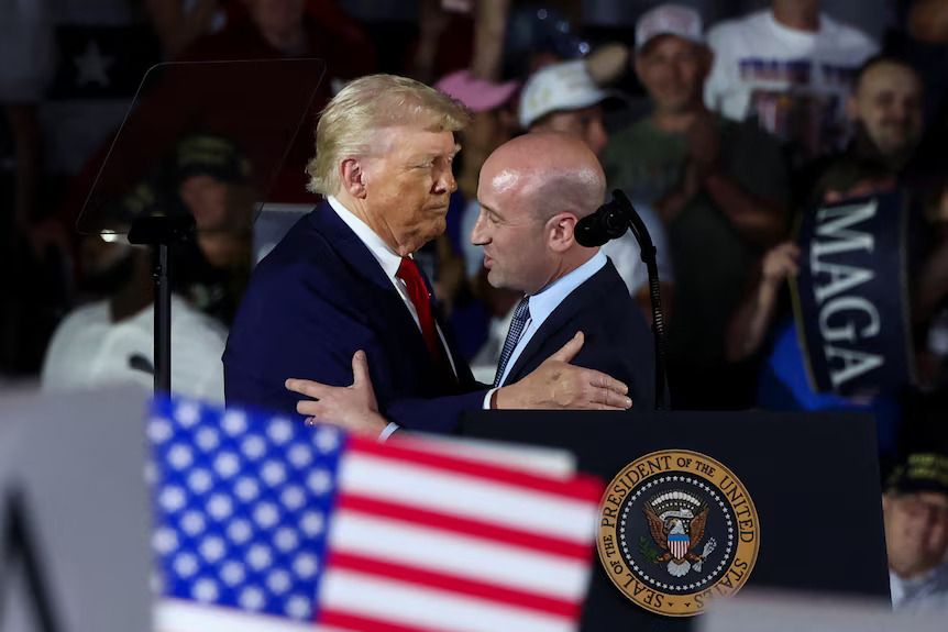 A photo of Donald J Trump and Stephen A.H. Miller at a podium with the seal of the Plenary President of the United States, embracing each other as they seek to take over the world. 