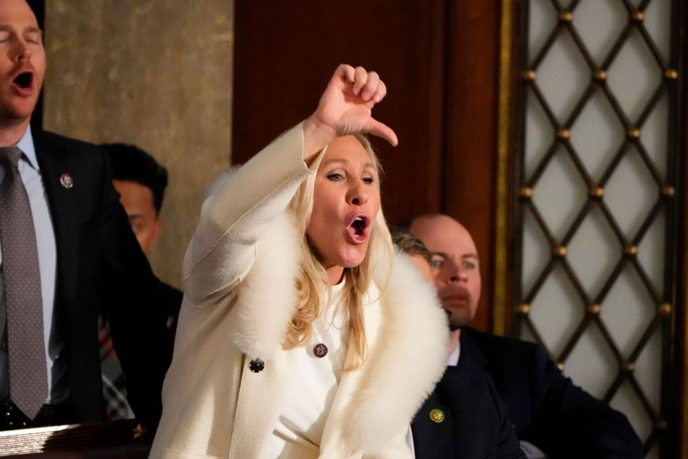 photo of marjorie taylor greene in white suit and white fur coat giving joe biden the thumbs down and loudly yelling “BOO!” and “LIAR!” during his 2023 SOTU address