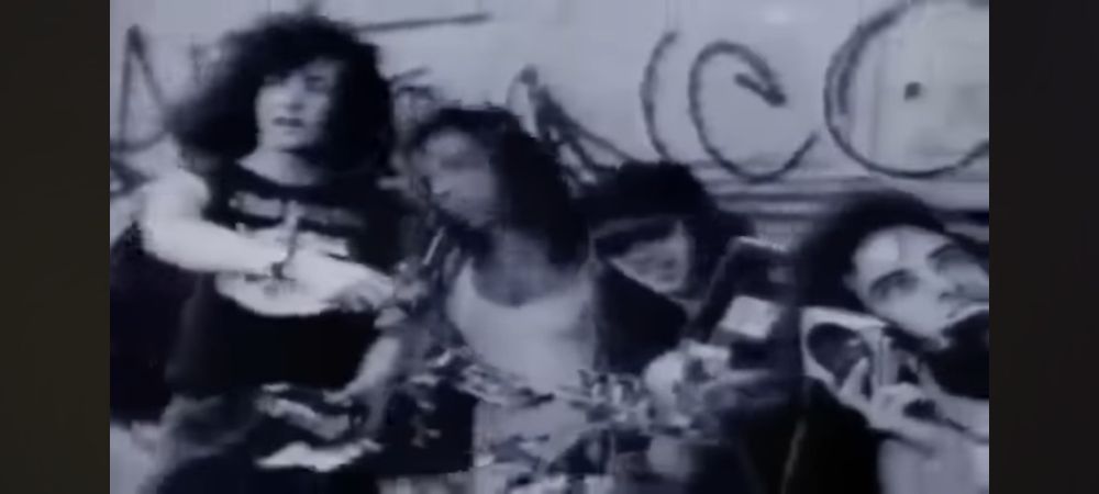 Four metal dudes against a graffiti wall with pieces of ghetto blaster everywhere, including in one person's mouth, making fun of vapid popular music. Still image from the video for "Brainwashed" by Nuclear Assault.