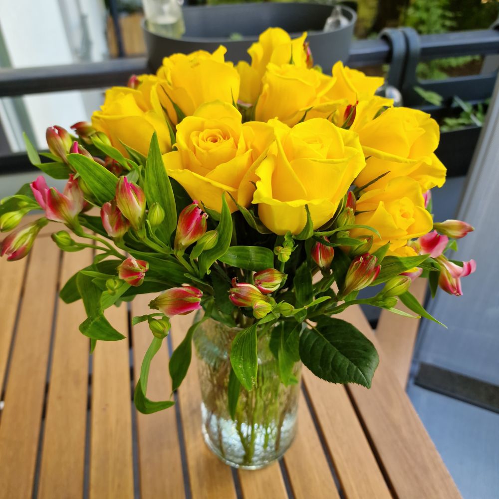 Gelbe Rosen und rote Alstroemeria in einer Vase, die auf einem Holztisch auf meinem Balkon steht.