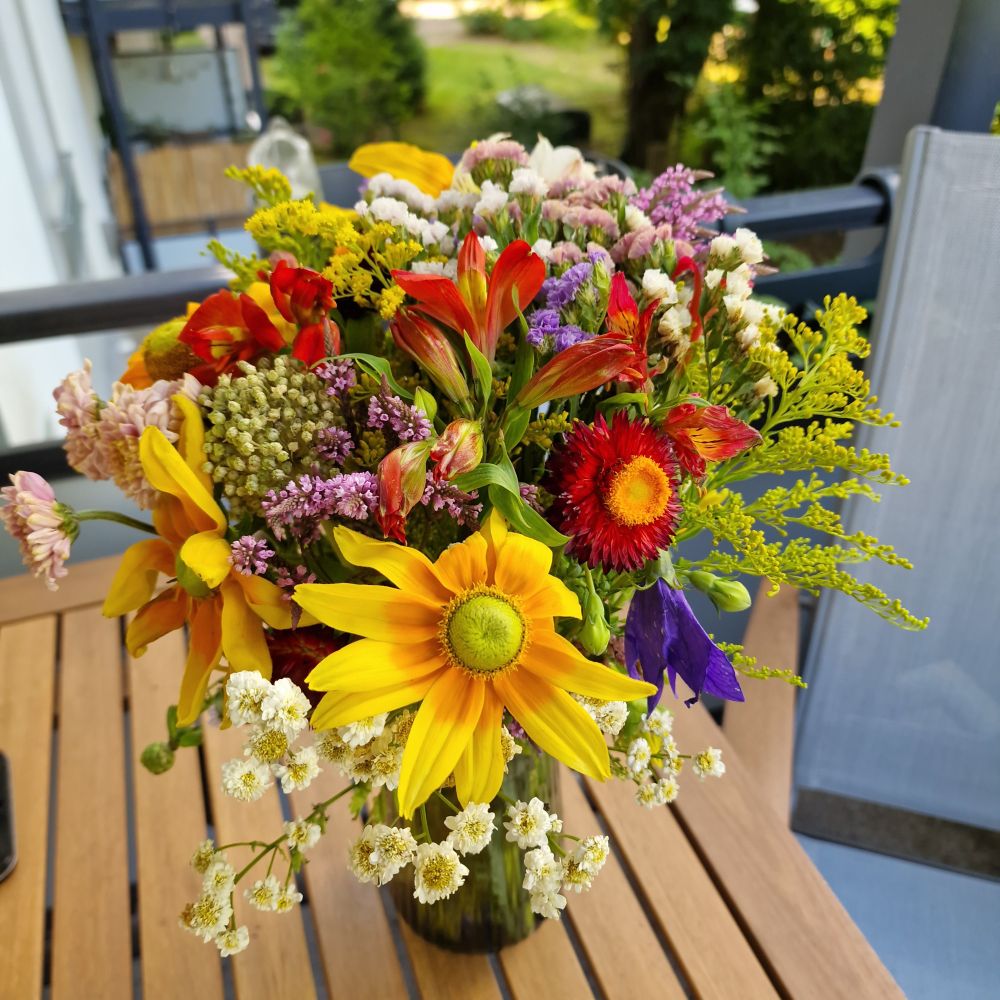 Wiesen-/Wildblumenstrauß mit vielen verschiedenen bunten Blüten, die ich in leider nicht bennen kann, da ich die Bezeichnung nicht kenne. Die Vase steht auf einem Holztisch auf meinem Balkon.