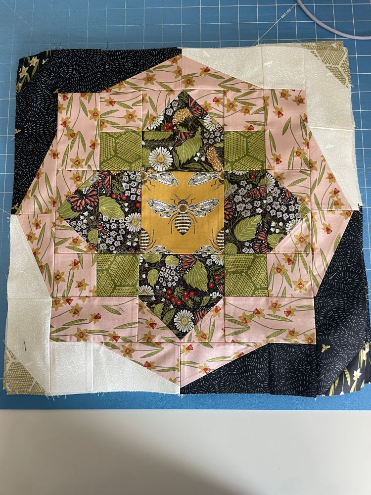 A quilt block of floral and bee fabrics featuring a black fabric near the center