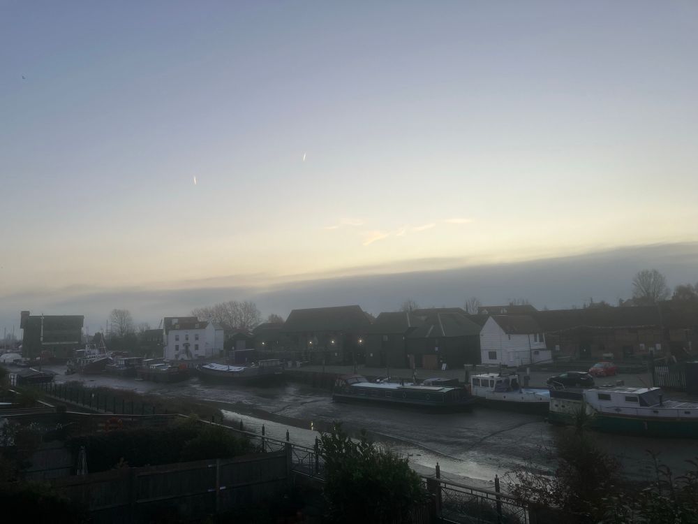 Lowlight behind a band of cloud across a pretty empty tidal creek and buildings 