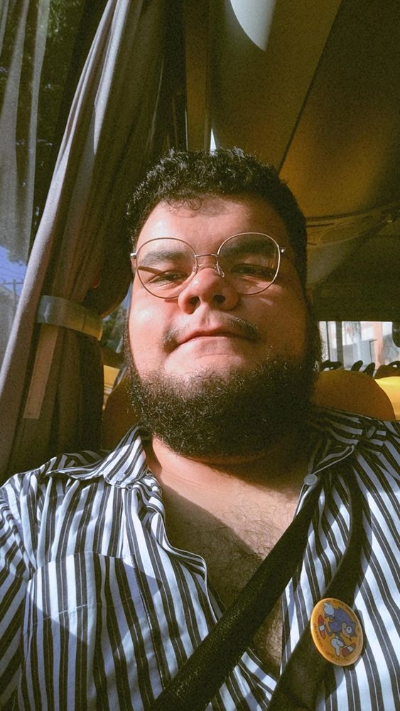selfie minha (homem branco, gordo, de barba e cabelo pretos, óculos redondo) usando uma camisa listrada com alguns botões abertos mostrando meu peito. estou olhando pra câmera com uma cara tranquila