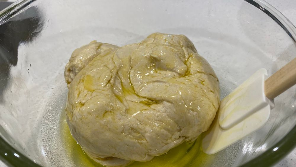 Pizza dough ball in olive oil resting in a glass bowl