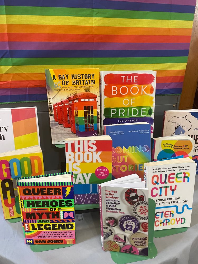Display of books on LGBT+ topics with very bright covers, in front of striped multicoloured fabric