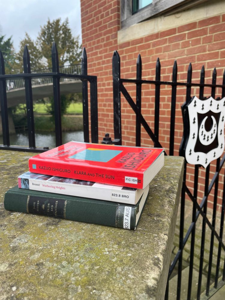 Pile of 3 books of the favourite books on a wall next to the river. The Trinity Hall logo is visible in the background