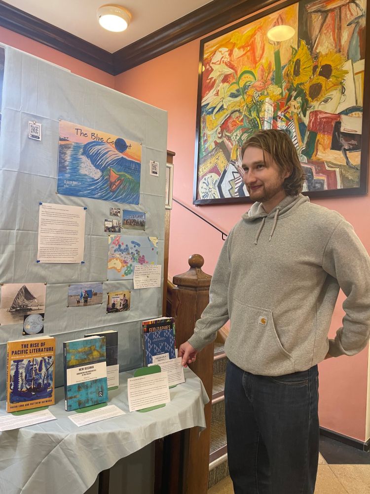 Man in grey hoodie stands next to a book display called the Blue continent