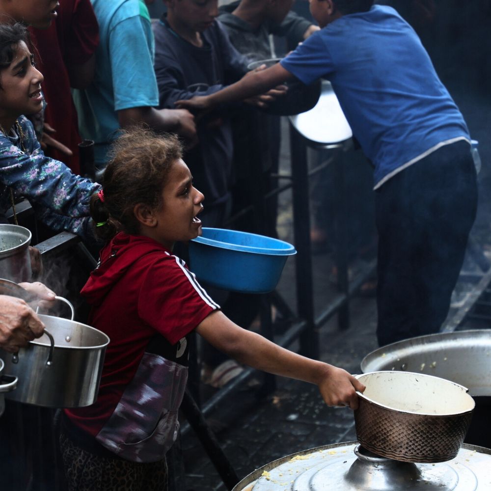 Photo of a girl with her hands outstretched at a food distribution point asking for food.