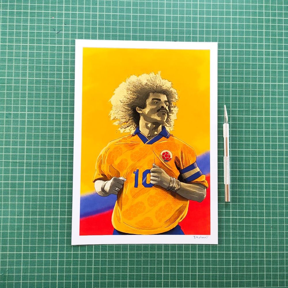 An upper body illustration of Carlos Valderrama in Colombia kit, yellow overlay with red and blue background stripe. Sitting on a green cutting matt.