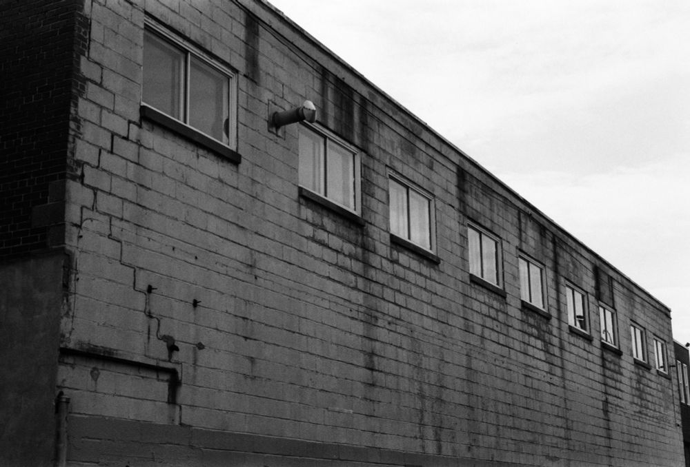 black & white: the side of a two-storey industrial building of large brick, with a row of windows along the second floor