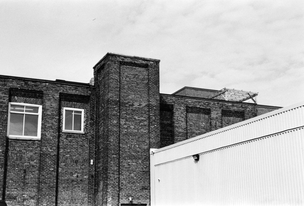 black & white: an old brick factory building, a cloudy sky, and a new corrugated metal building