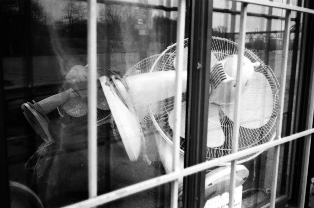 black & white: a pile of white table fans behind the window of a parking booth